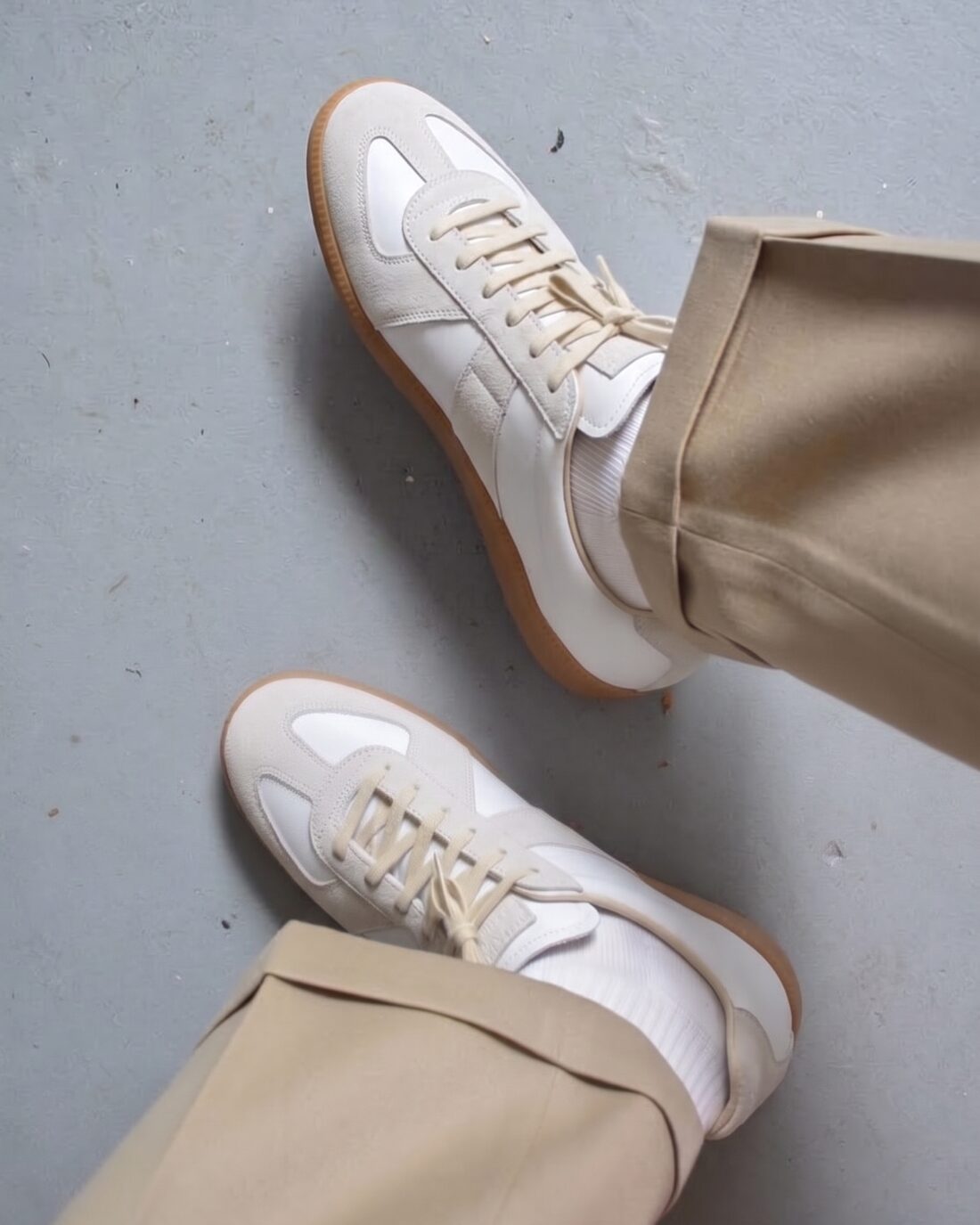 Flat white sneakers with gum soles under a beige trouser hem